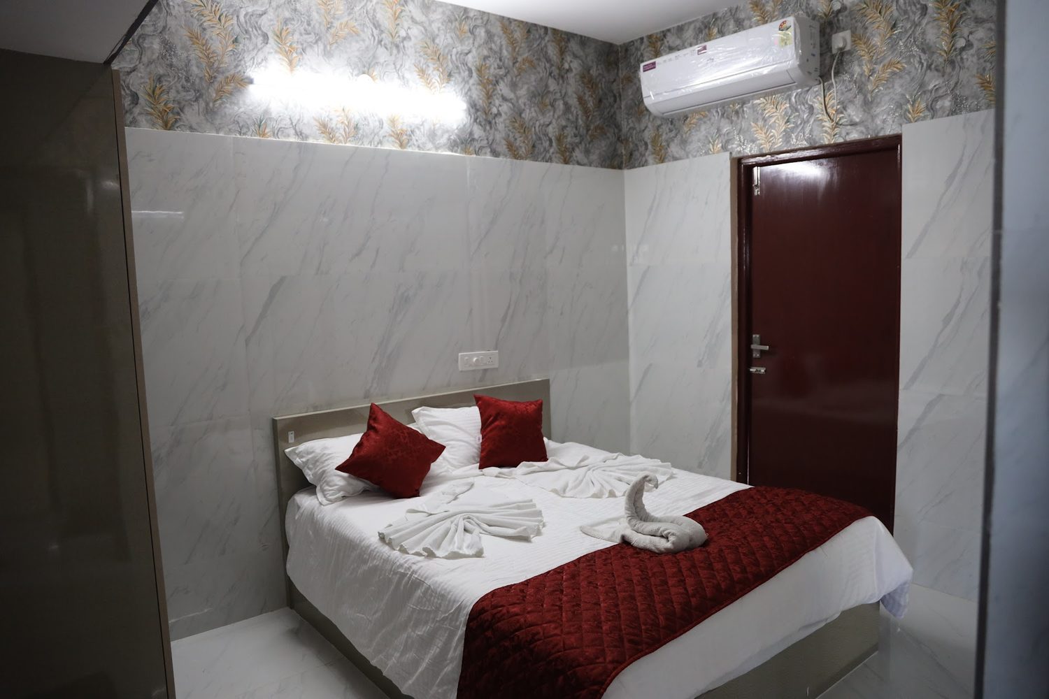 A double bed made up with white linen, a maroon throw and towels folded on the bed.