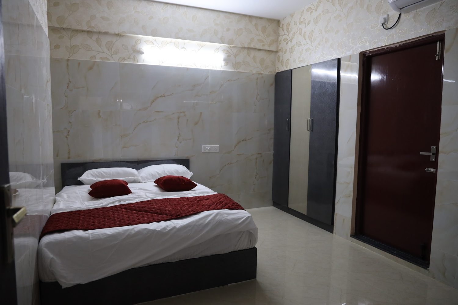 A bedroom with a double bed, a run of tall wardrobes and a maroon door.