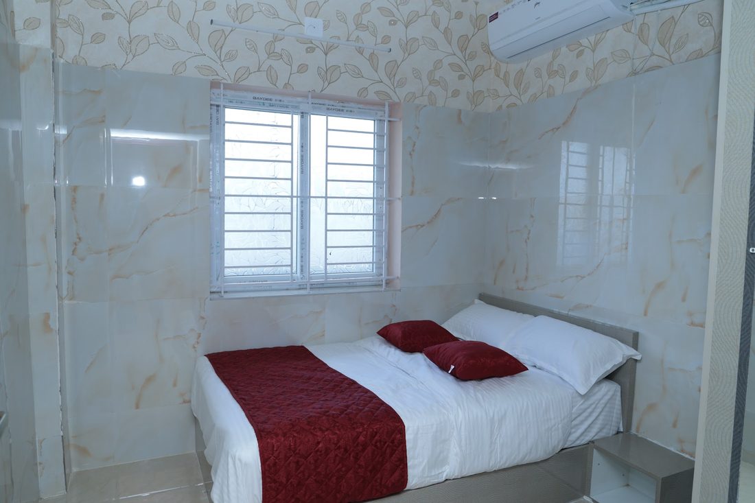 A bright bedroom with louvred windows throwing light across a double bed.