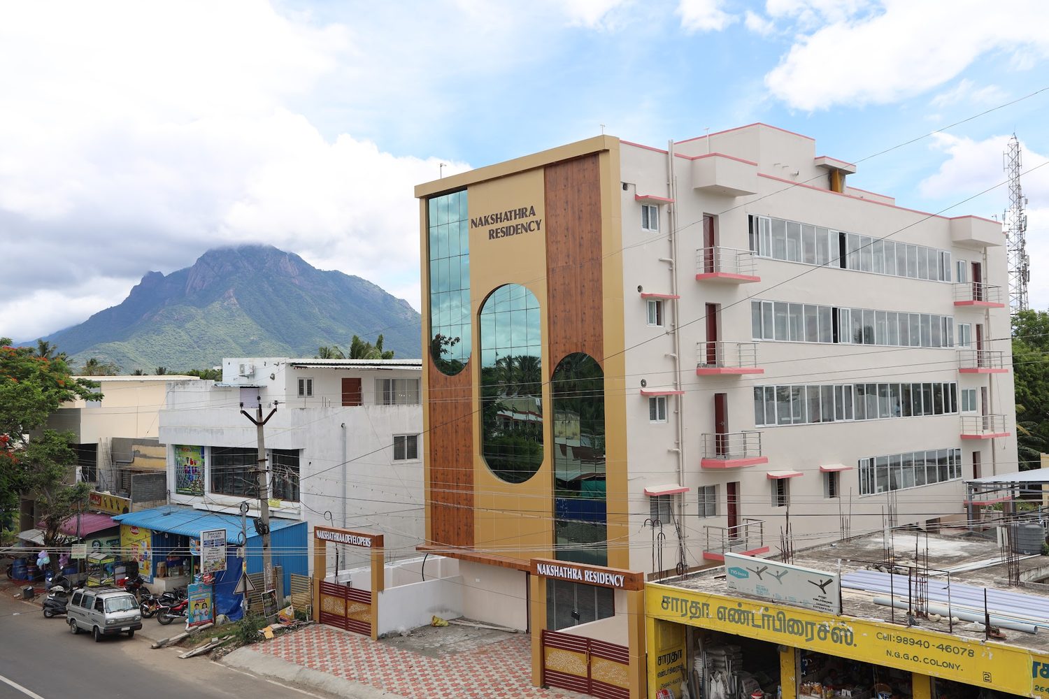 Nakshathra Residency from across the road, with the hill behind it and shops at street level.