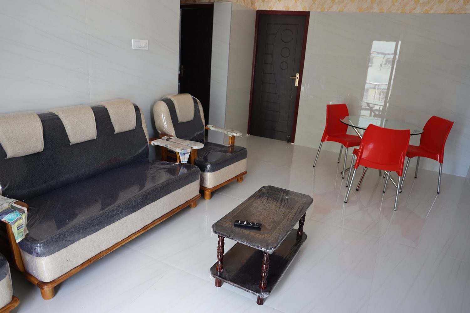 An apartment living room with a long sofa, a wooden coffee table and red moulded chairs by the window.