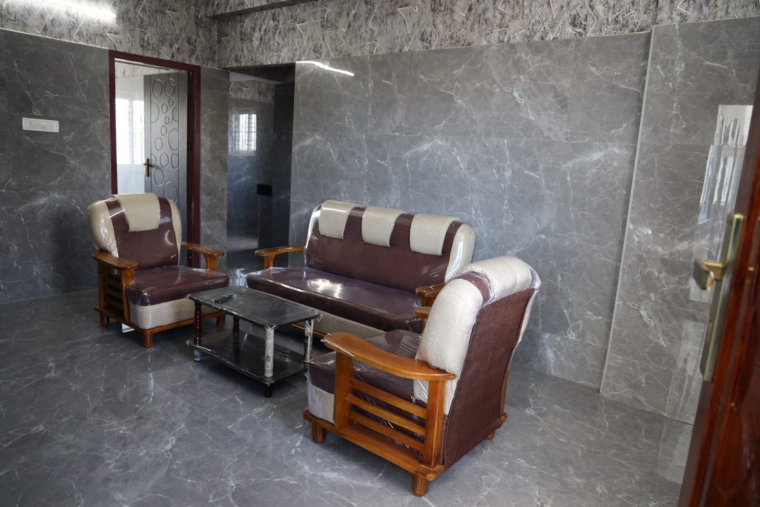 A sitting area with two armchairs and a sofa around a glass-topped table against a grey marble wall.