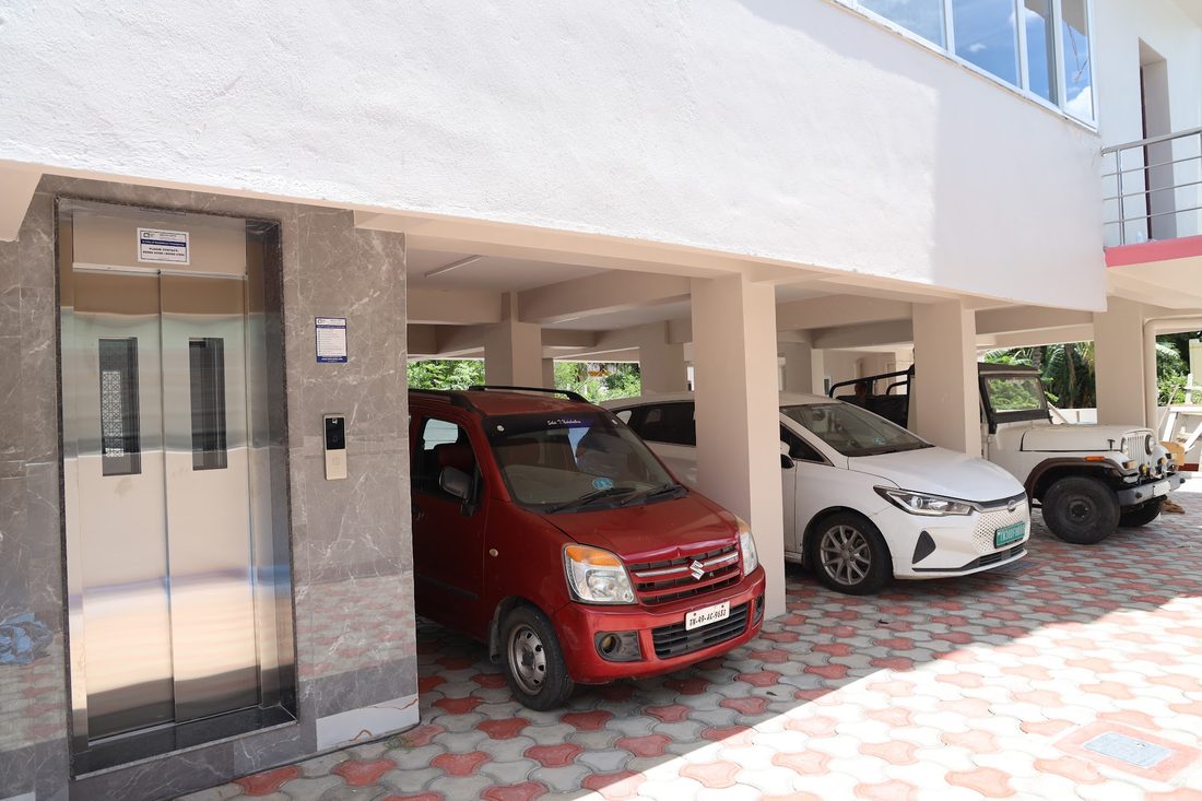 Covered parking under the building with a car and two-wheelers on a patterned paver floor beside the lift door.