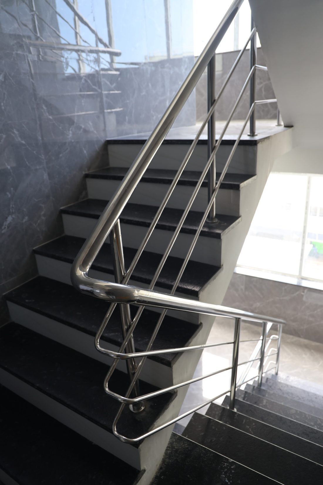 The main staircase with a stainless steel handrail and a tall window at the landing.